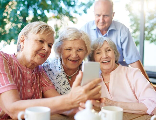 A group of seniors looking at a phone smiling and interested.
