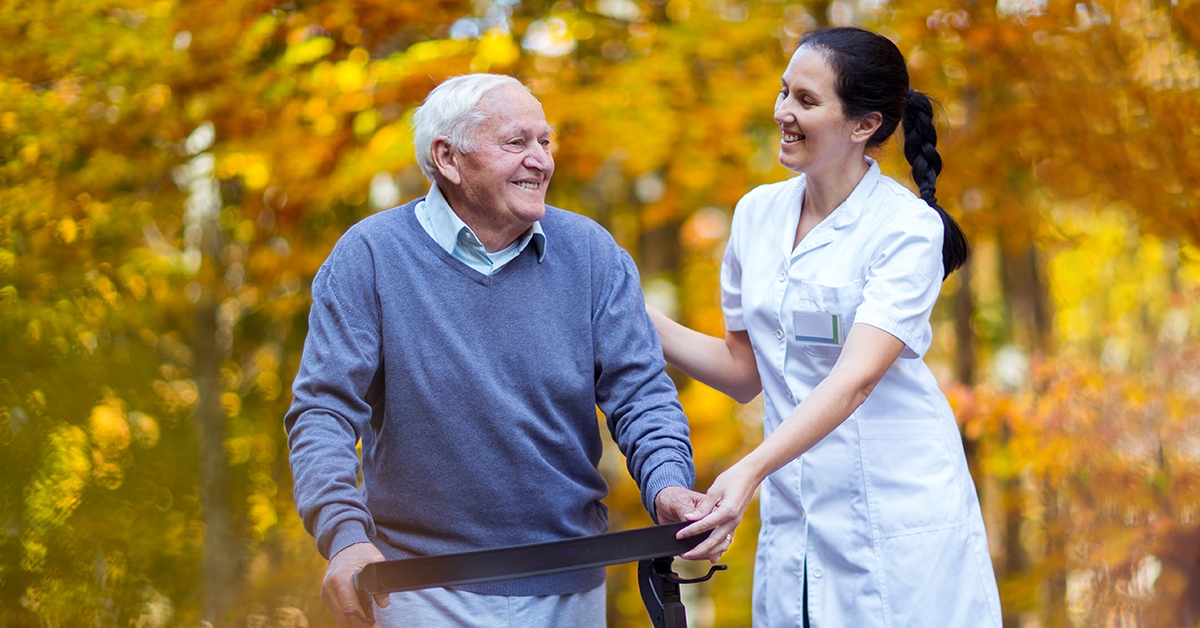 Senior man using a walker with a nurse assisting him