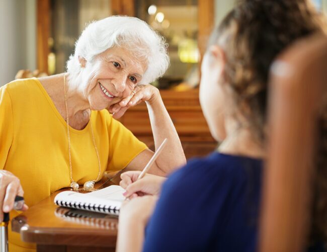senior woman smiling at a young child writing in a book