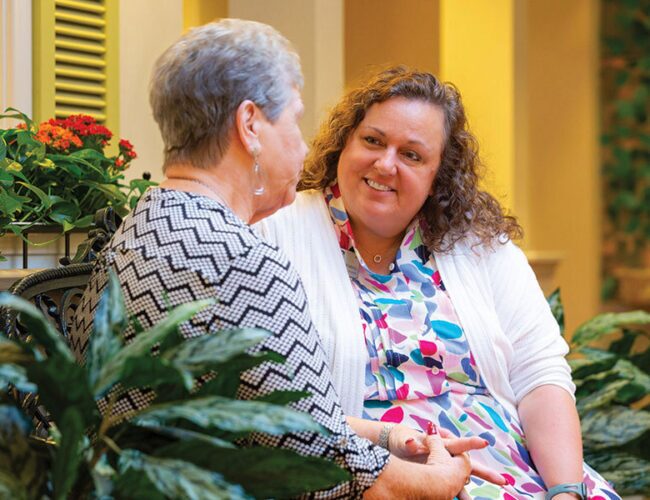 A caregiver sits and speaks with a resident in the village.