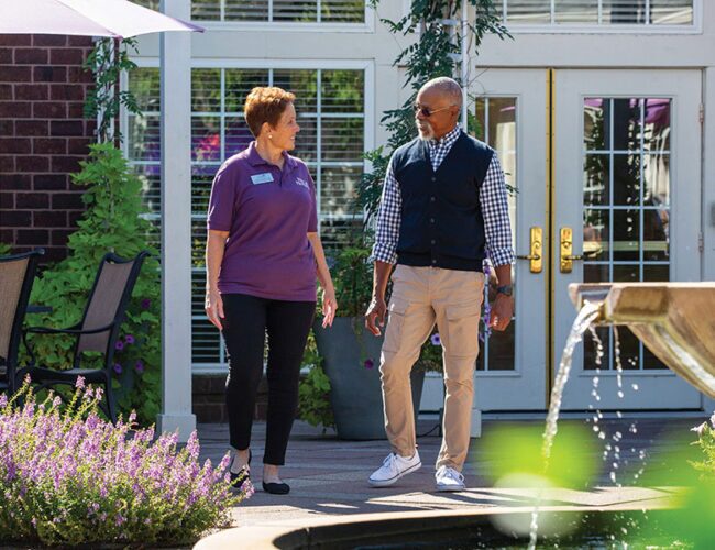 A registered nurse walking with a senior in a park-like setting.
