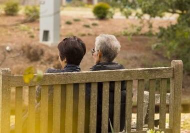 adult daughter and senior mother sitting on a park bench