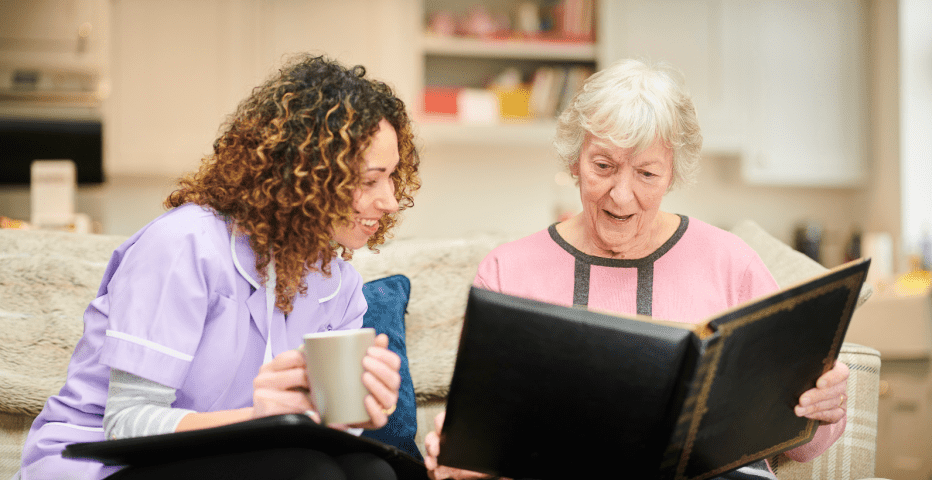 senior woman holding a photo album with a nurse glancing over to look at it