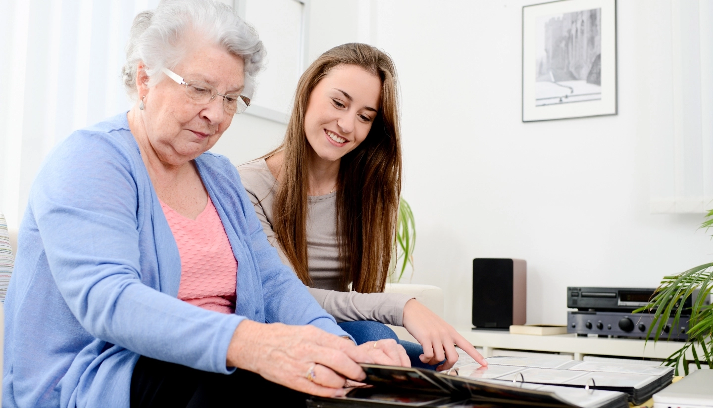 Young woman and elderly relative happily looking at a photo album.