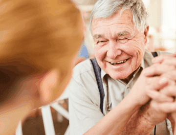 An older man holds hands with somebody and smiles.