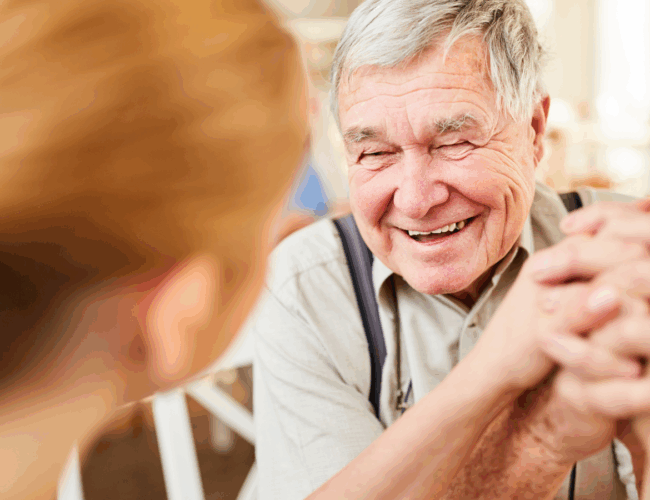 An older man holds hands with somebody and smiles.