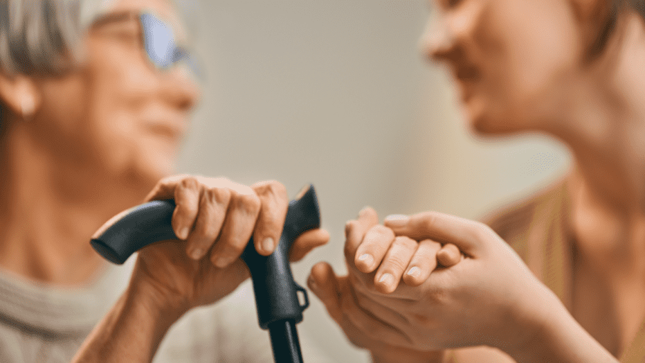 senior woman holding hands with a younger woman while holding a cane
