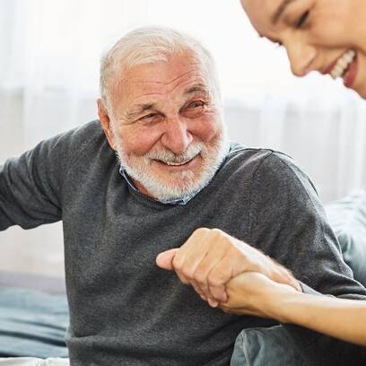 A caregiver and resident holding hands and smiling.