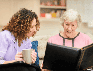 senior woman holding a photo album with a nurse glancing over to look at it