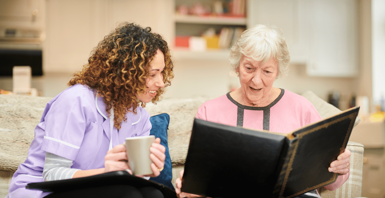 senior woman holding a photo album with a nurse glancing over to look at it