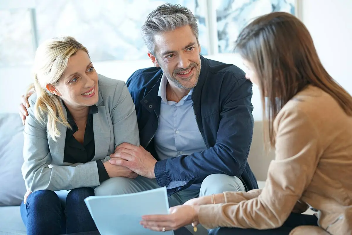 A husband and wife hold each other as they speak to a consultant. They are smiling.