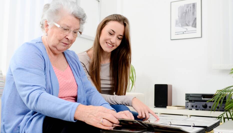Young woman and elderly relative happily looking at a photo album.