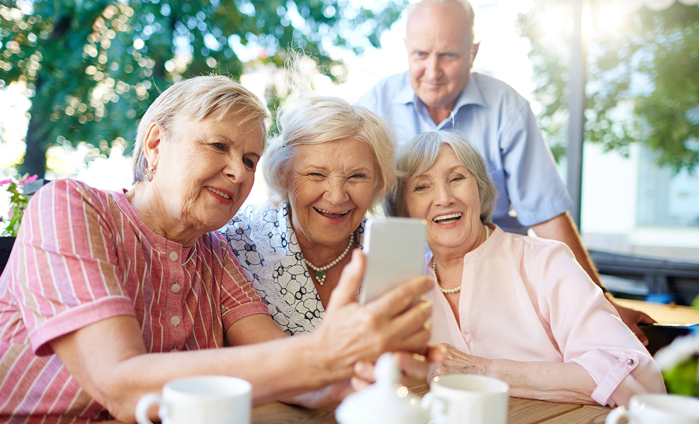 A group of seniors looking at a phone smiling and interested.