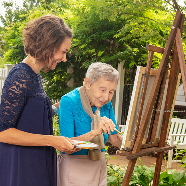 A young woman painting outside with an older woman