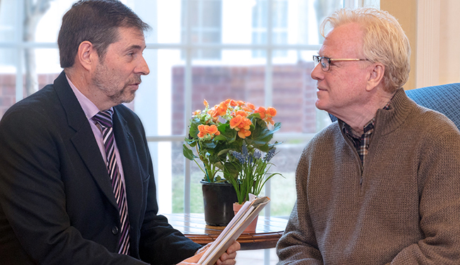 Two men, one in a suit and one in a 3/4 zip, having a conversation