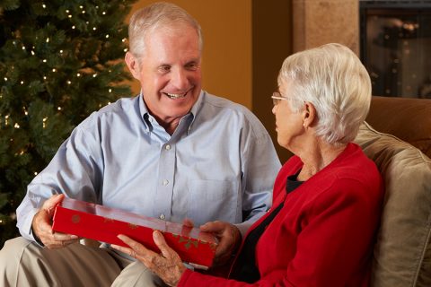 A man and a woman sit on a couch exchanging a holiday gift