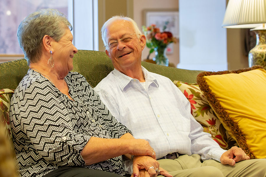 A couple seated on a sofa looking at each other smiling.