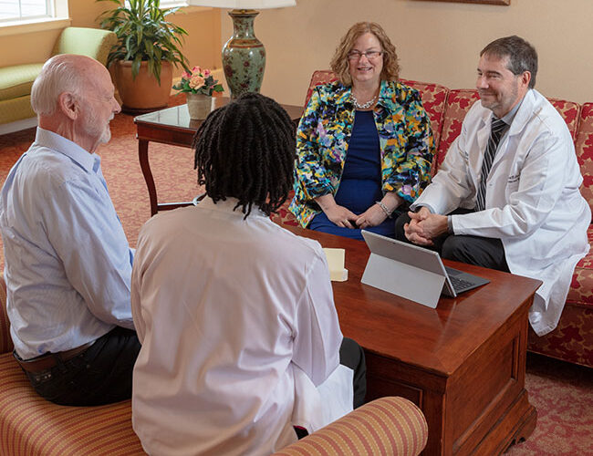 Doctors speak to resident on sofa.