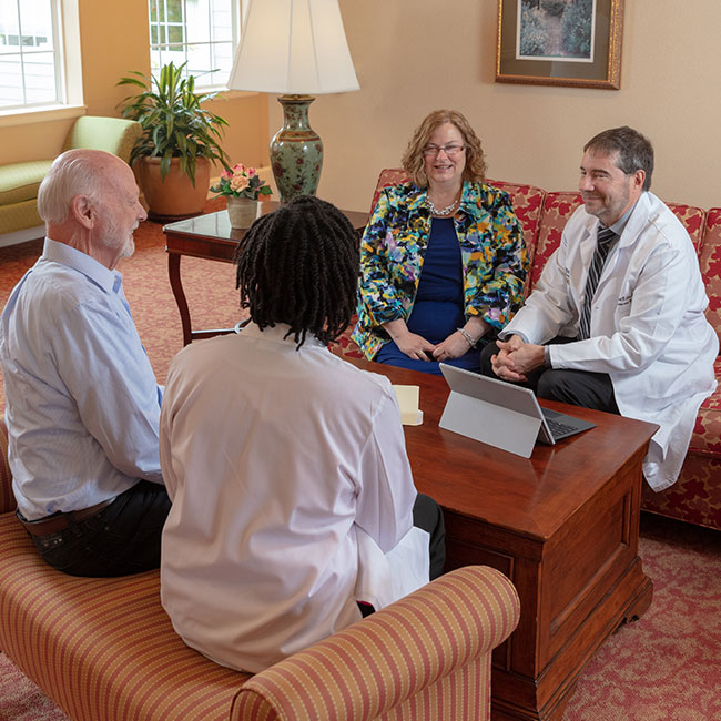 Doctors speak to resident on sofa.