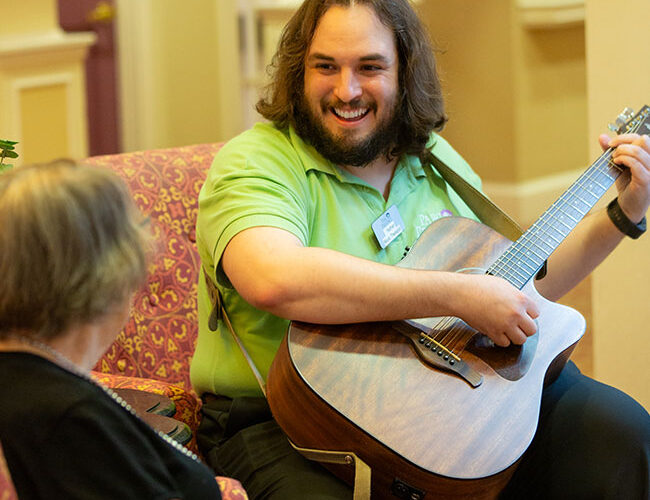 A caregiver playing the guitar for a resident.