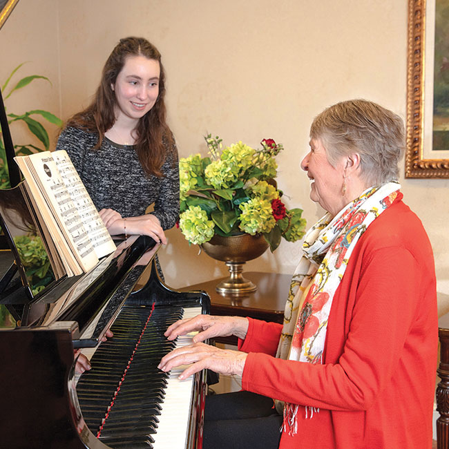 A resident plays the piano while a young woman stands and admires.