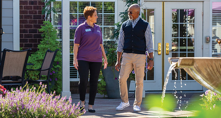 A registered nurse walking with a senior in a park-like setting.