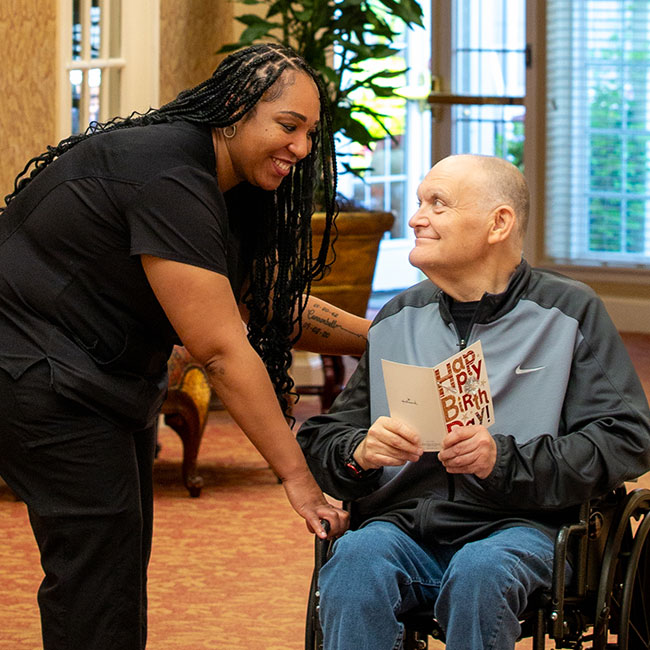A caregiver and a resident in a wheelchair with a birthday card.