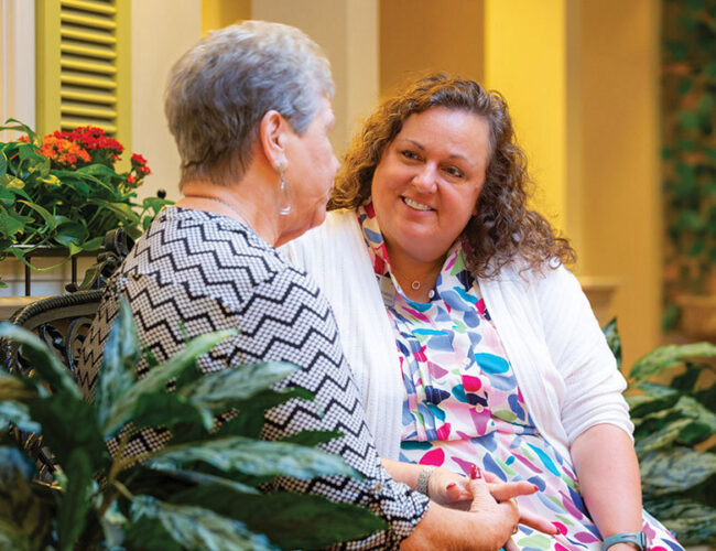 A caregiver sits and speaks with a resident in the village.