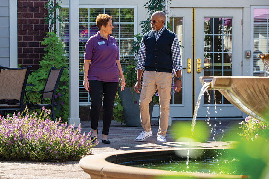 A registered nurse walking with a senior in a Parc Provence courtyard.