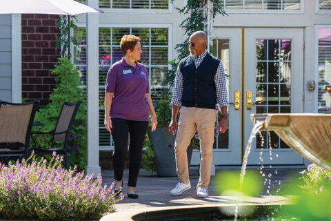 A registered nurse walking with a senior in a park-like setting.