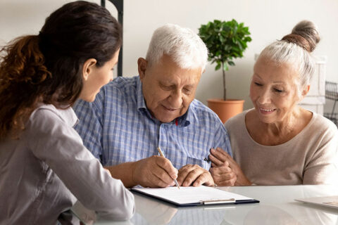 A man signing a document as a worker and an wife look on.