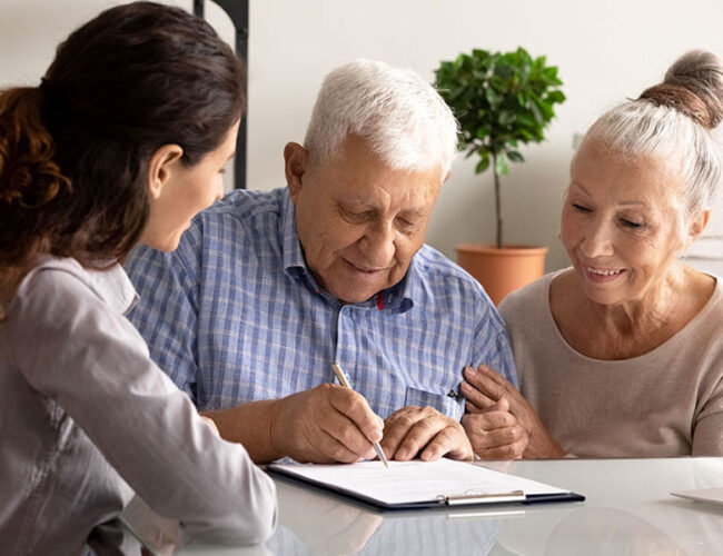 A man signing a document as a worker and an wife look on.