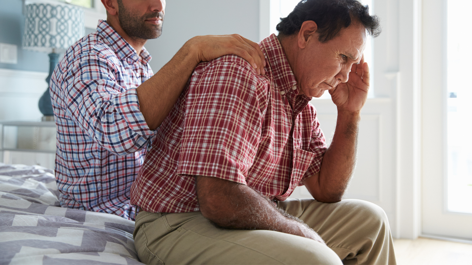 Man with hand on shoulder of another man who is showing signs of depression.