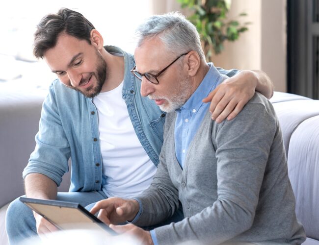 Young man with elderly male relative smiling while looking at a framed image.