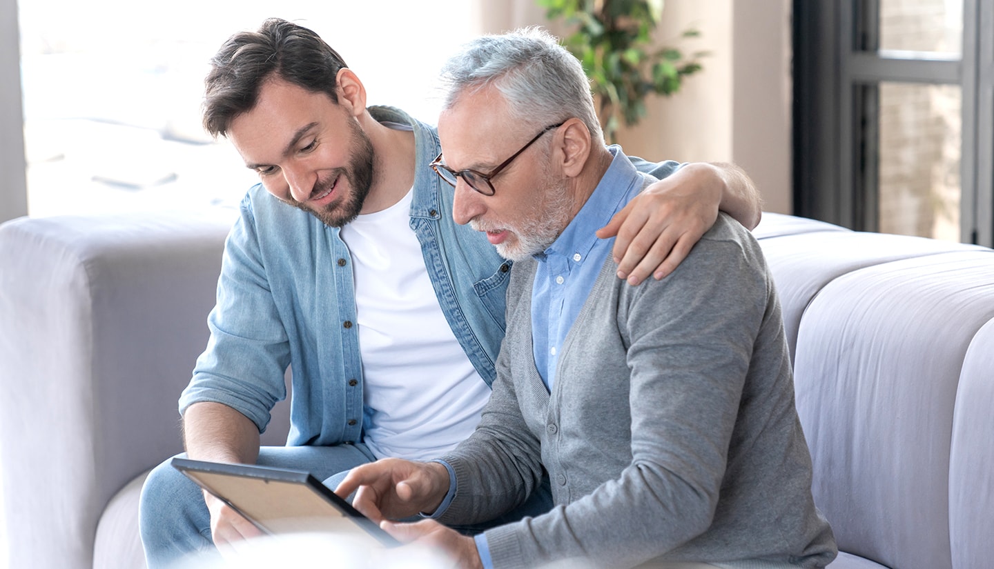 Young man with elderly male relative smiling while looking at a framed image.
