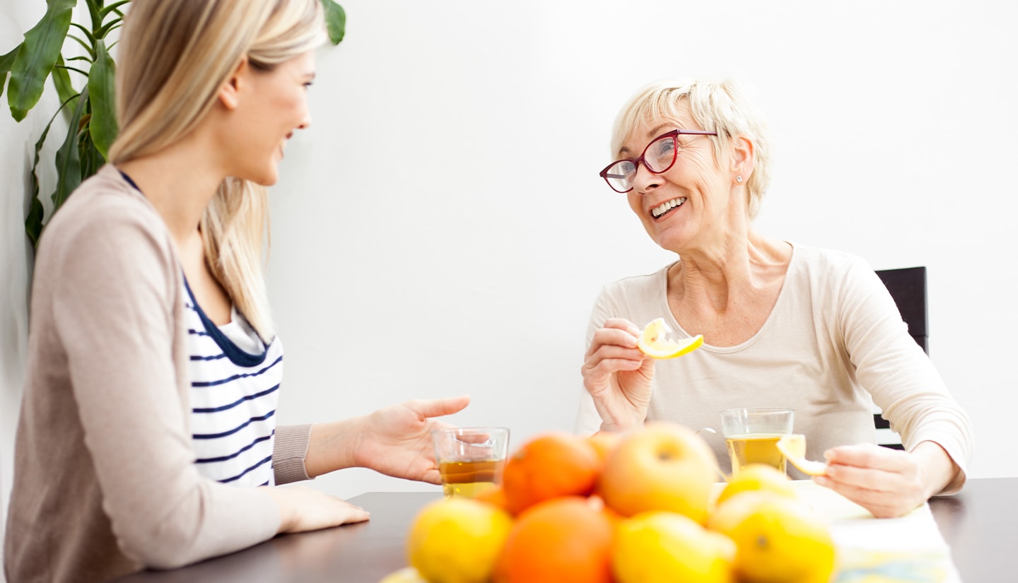 Young woman and elderly woman conversing at table with fruit and iced tea.