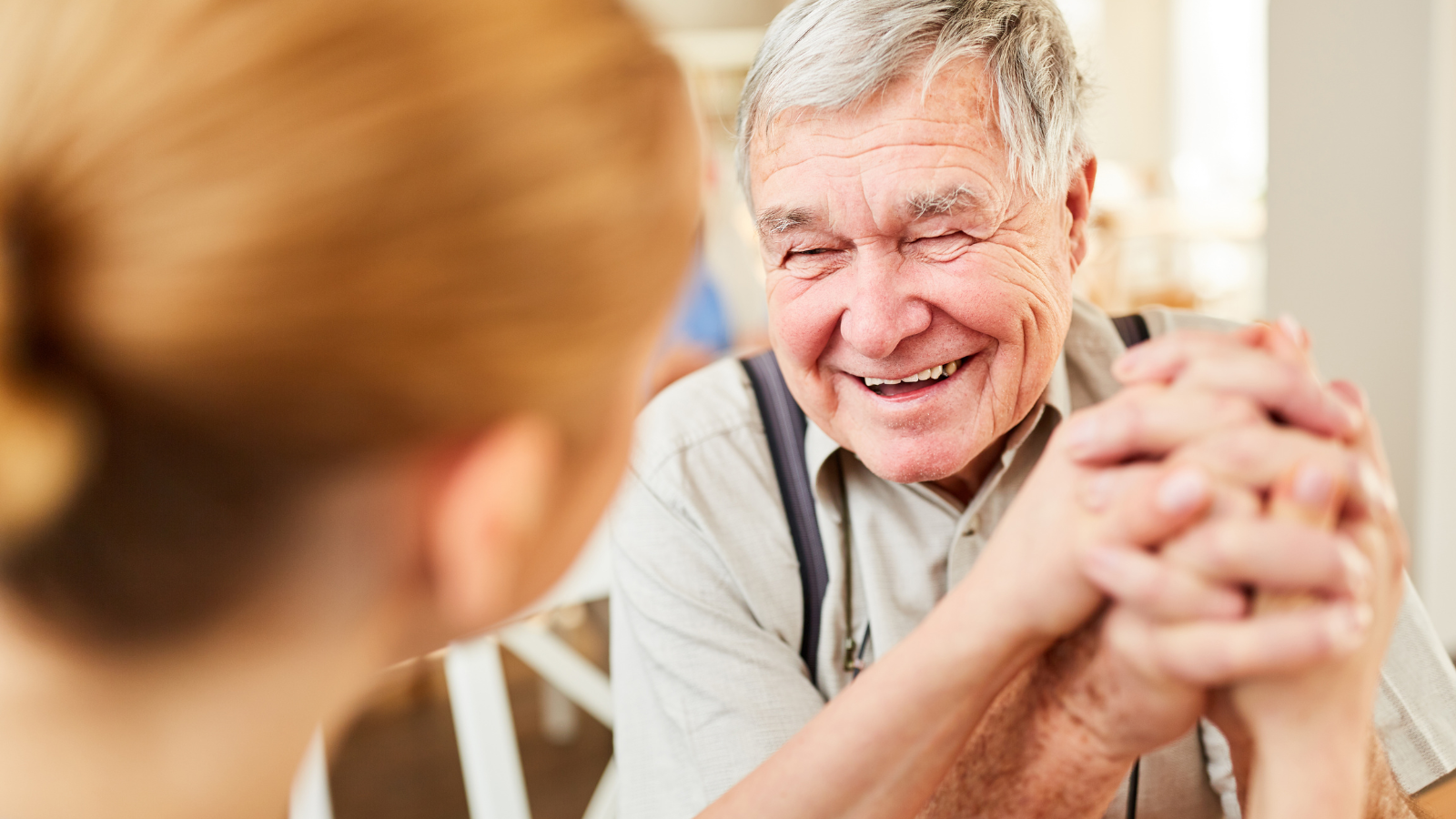An older man holds hands with somebody and smiles.
